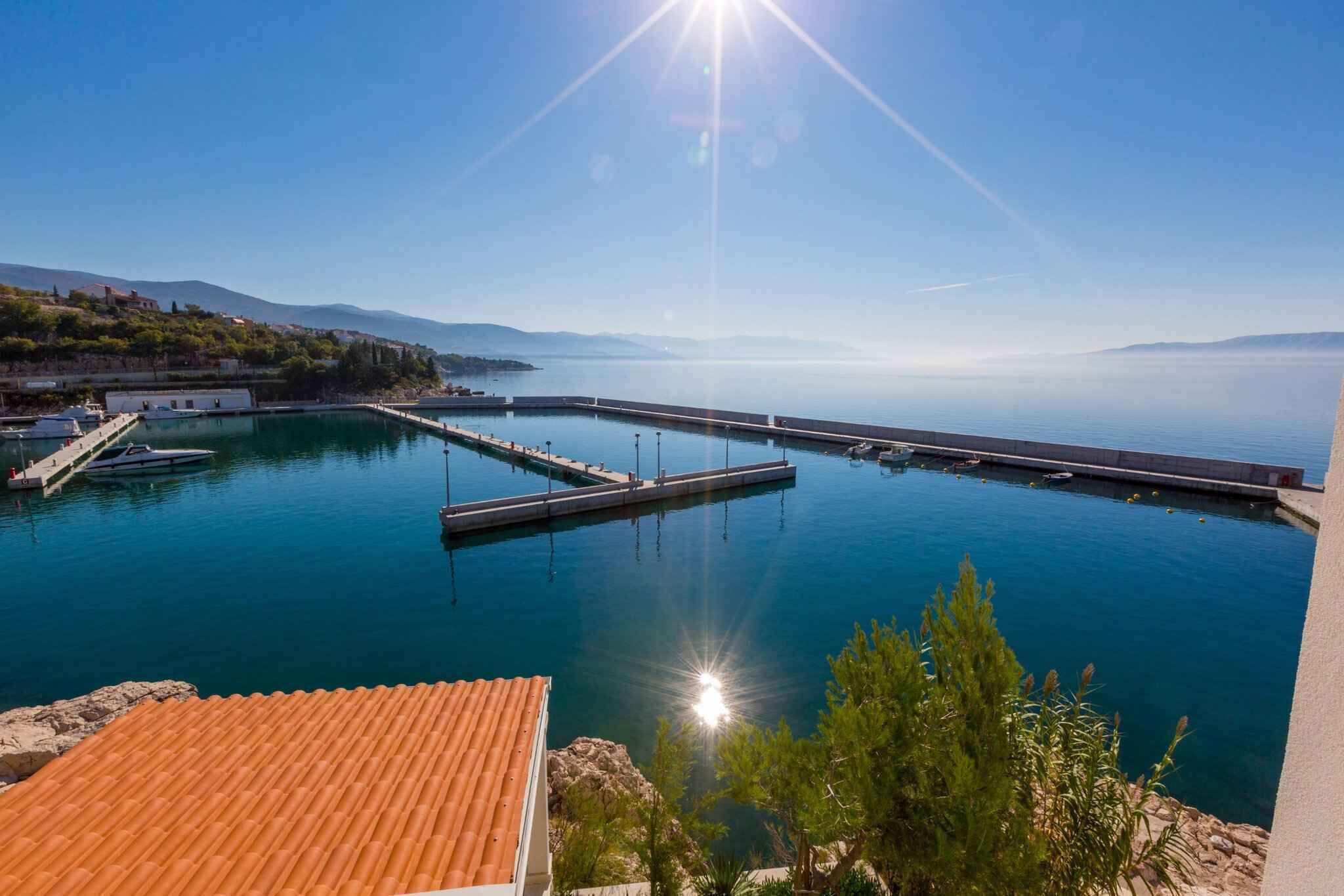 Ein Yachthafen mit vertäuten Booten, eine Pier, die sich in ruhiges Wasser erstreckt, und ein klarer Himmel.