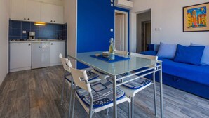 Una cocina moderna con armarios blancos y baldosas azules, una mesa de comedor de vidrio con sillas, y un sofá azul en la sala de estar.