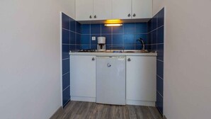 Una cocina compacta con armarios blancos, una cafetera y un lavabo.