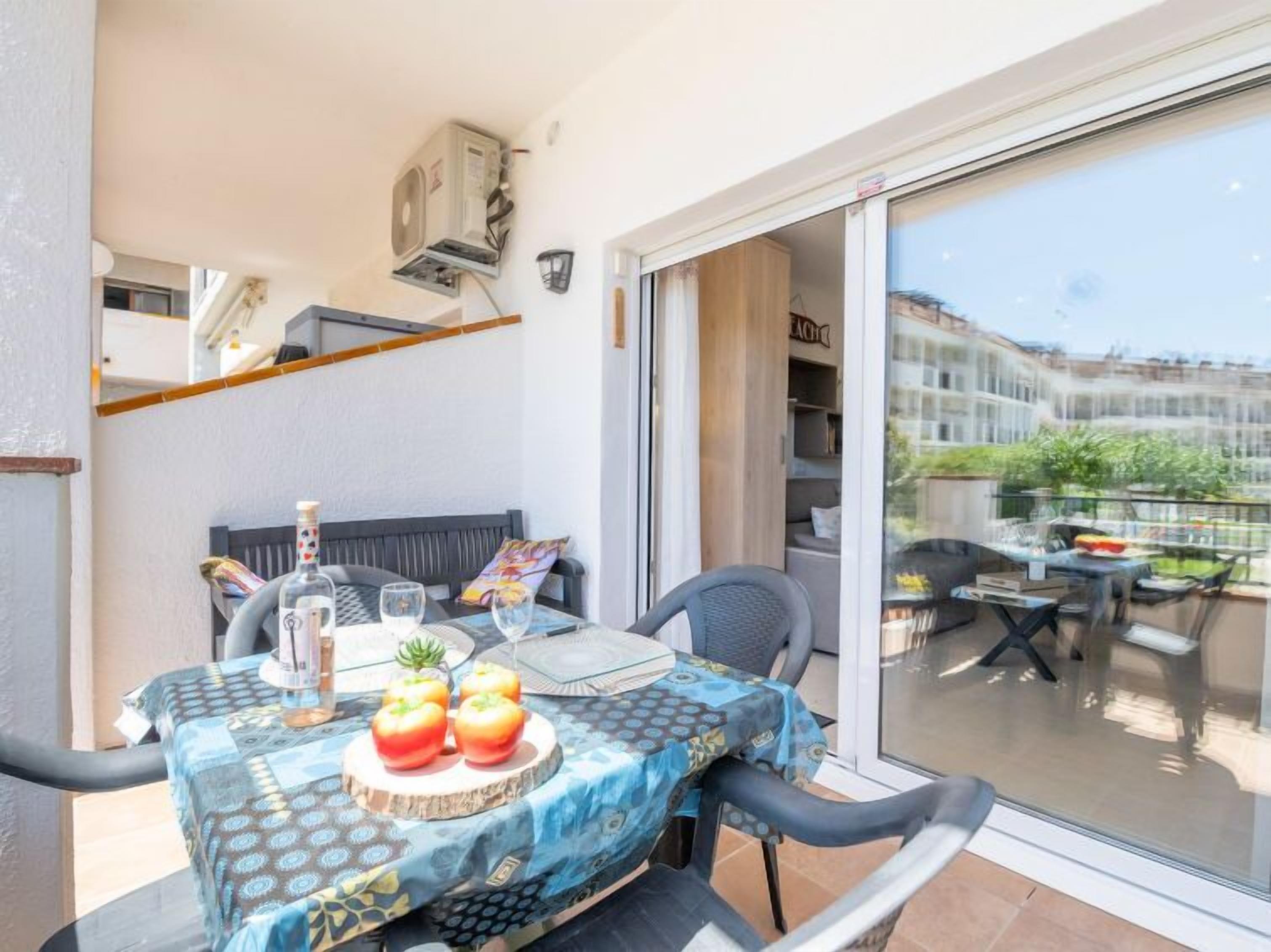 A balcony with a table set for two, featuring a tablecloth, a bottle, glasses, and apples.