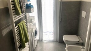 Un baño con inodoro, ducha, tendedero con toallas y lavadora.