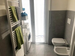 A bathroom with a toilet, a shower, a drying rack with towels, and a washing machine.