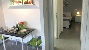 Un comedor con una mesa dispuesta para dos, un cuadro en la pared y vistas a un dormitorio con cama y mesita de noche.