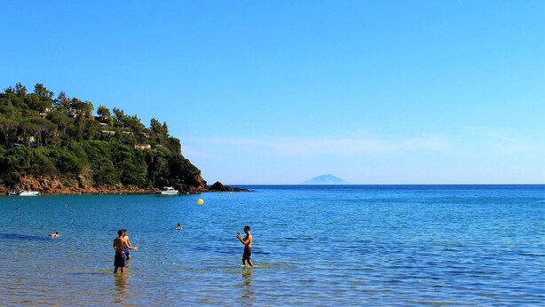 A coastal scene with clear blue water, a small boat, and people in the water.