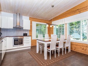 A modern kitchen with white cabinets, a stove, and a large window overlooking a forest. - Vacation home Kaisla by Interhome (Heinola)