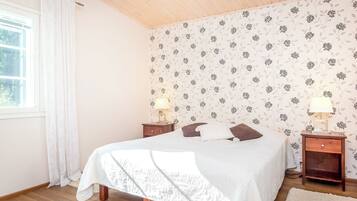 Une chambre à coucher avec un lit, deux tables de chevet, une fenêtre avec des rideaux et un papier peint à motifs floraux.
