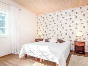 A bedroom with a bed, two bedside tables, a window with curtains, and a floral wallpaper. - Vacation home Kaisla by Interhome (Heinola)