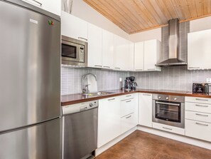 A modern kitchen with stainless steel appliances, white cabinetry, and a wooden ceiling.