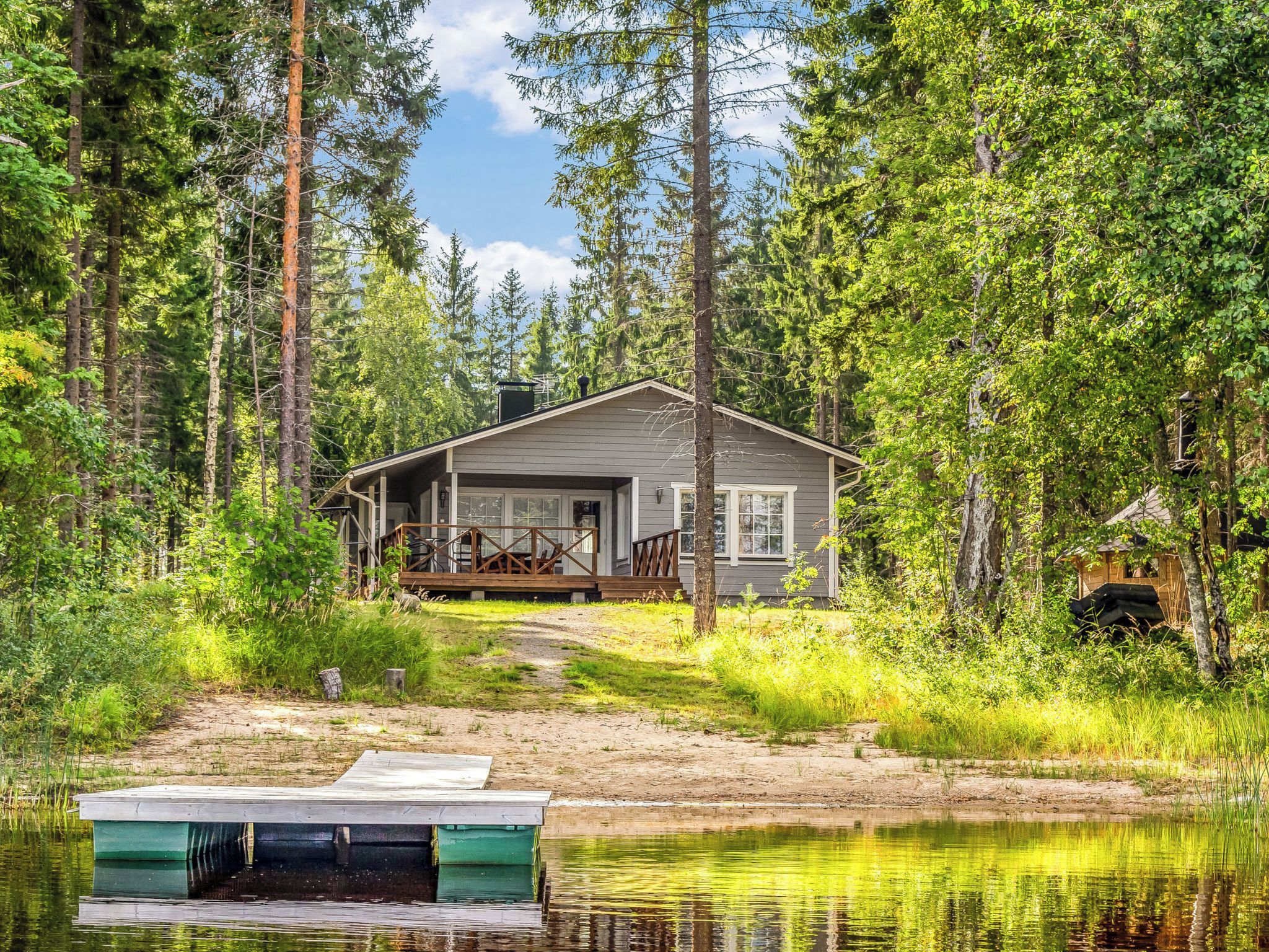 Une cabane dotée d’une terrasse, entourée de forêt et bordée par un plan d’eau.