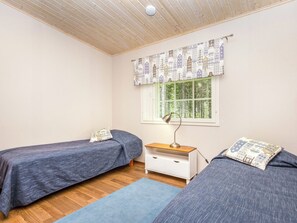 A bedroom with two single beds, a nightstand, a lamp, a window with a view of trees, and a ceiling with wooden beams. - Vacation home Kaisla by Interhome (Heinola)