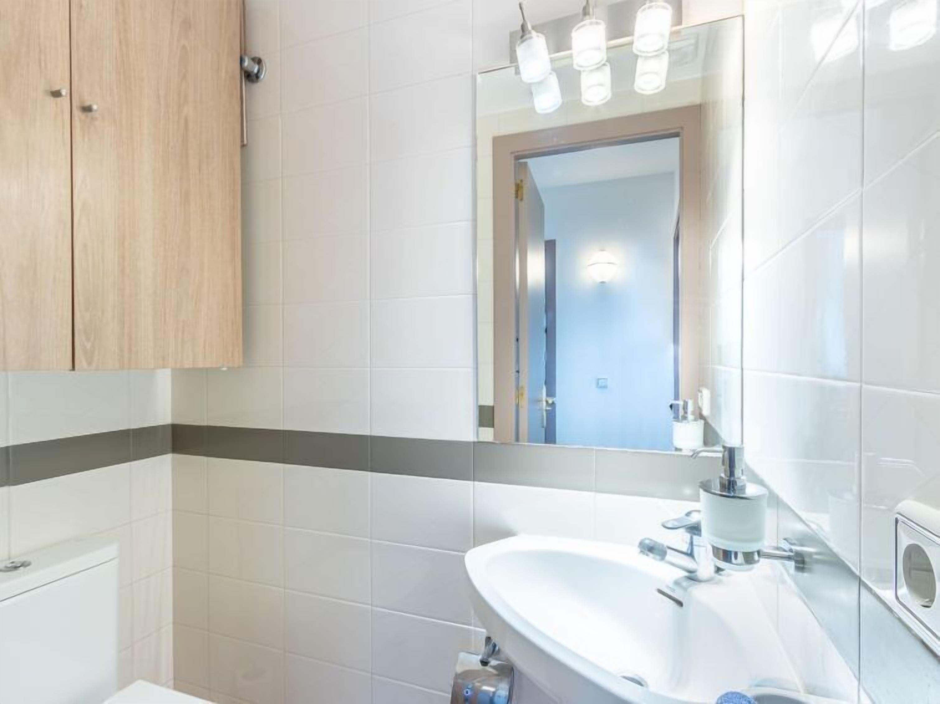 Een moderne badkamer met een wit wastafelmeubel, spiegel en verlichtingsarmaturen.