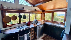 A compact kitchen with a gas stove, a coffee maker, and hanging pots.
