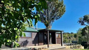 A wooden cabin with a covered porch, surrounded by a gravel path and greenery.