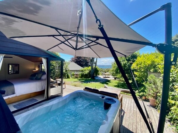 A hot tub with a wooden deck, a bed with a view, and a patio umbrella.