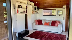A cozy living room with a white sofa, red and white cushions, a red patterned rug, and built-in shelving with various items.