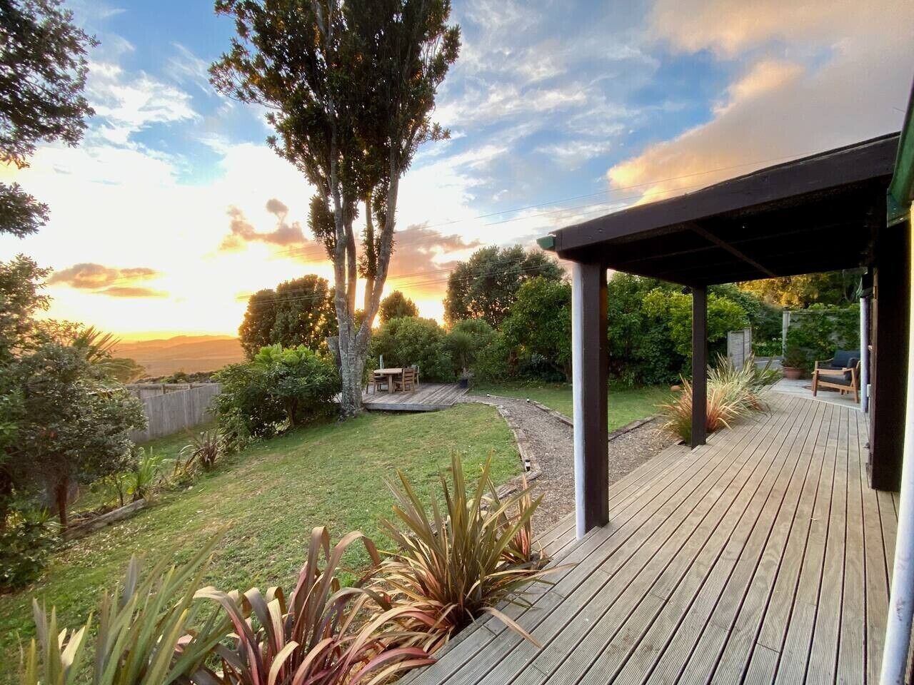 A wooden deck with a covered seating area, surrounded by a well-maintained garden and a view of the sunset.
