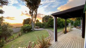 A wooden deck with a covered seating area, surrounded by a well-maintained garden and a view of the sunset.