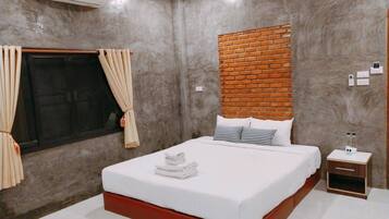 Un dormitorio con una cama grande, una pared de ladrillo decorativa, un equipo de aire acondicionado, una ventana con cortinas y una mesita de noche con una botella.