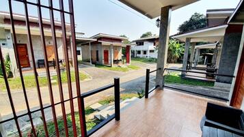 A balcony with a view of a residential street, featuring houses with red doors and a covered walkway.
