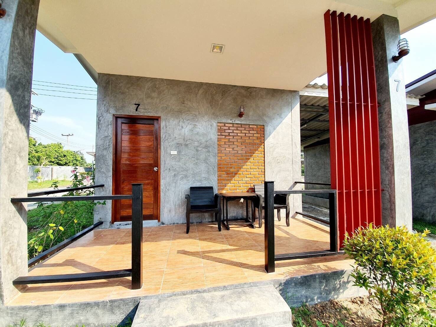 A covered outdoor area with a wooden door marked with the number 7, a brick wall, and a red vertical structure.