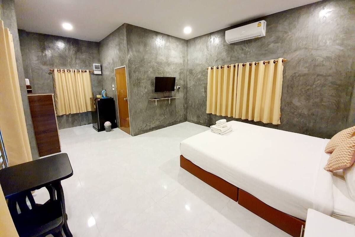 A modern hotel room with a large bed, a desk, a TV, and a bathroom with a shower and toilet.