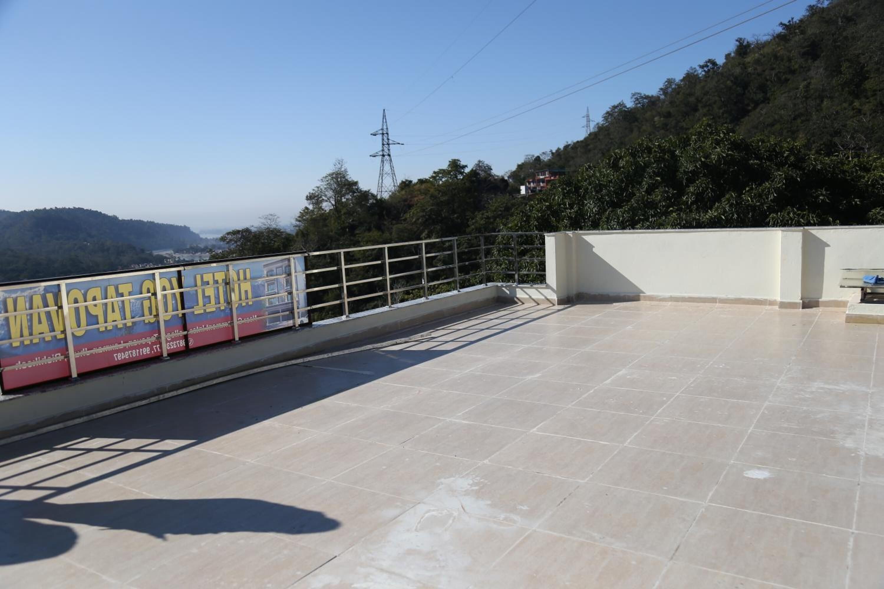 Terraza en la azotea con suelo de baldosas, barandilla de metal y un cartel publicitario de un hotel.