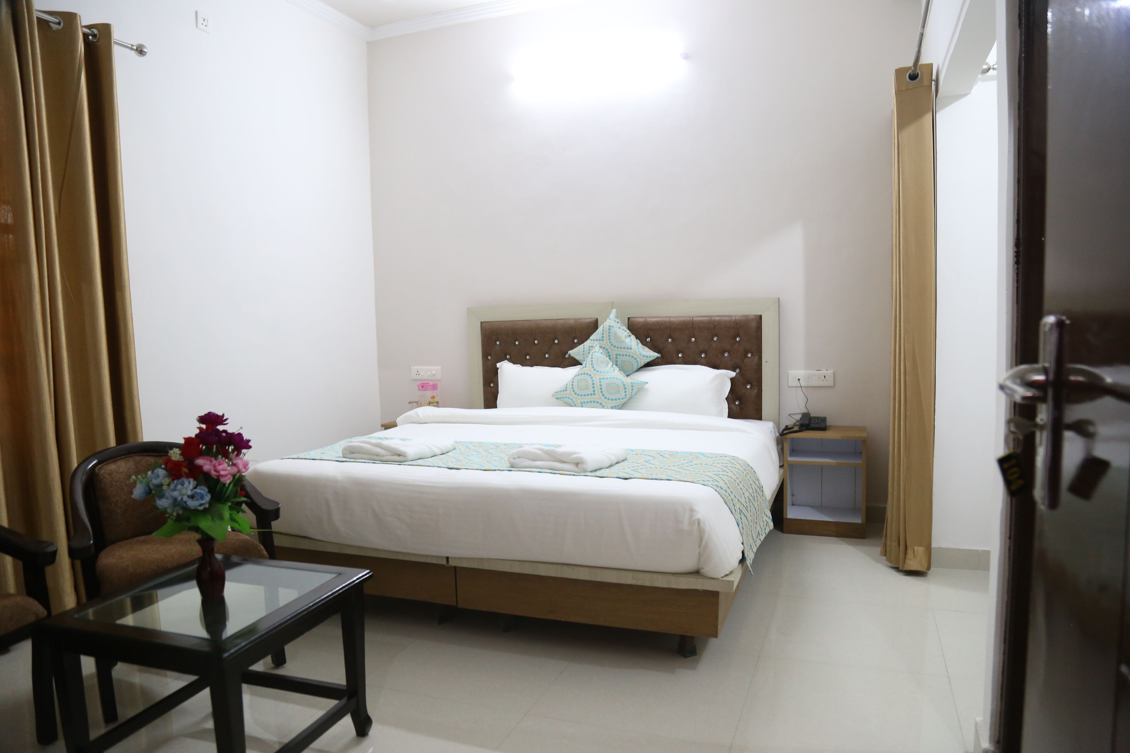 A hotel room with a bed, a small table with a vase of flowers, a chair, a nightstand, and a wardrobe.