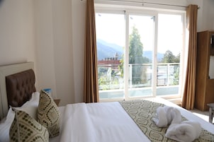 A hotel room with a large bed, a headboard, a window with curtains, and a view of mountains and a pool.