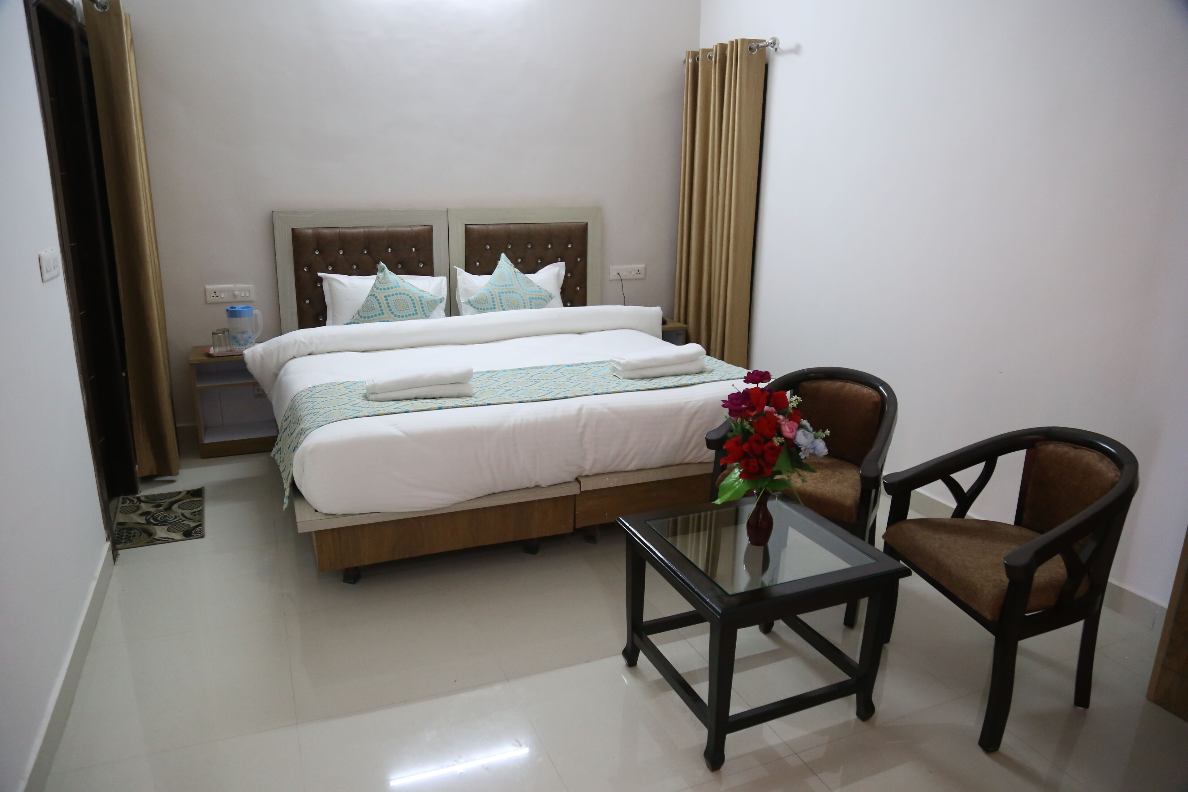 A hotel room with a bed, bedside table, chair, and a small table with a vase of flowers.