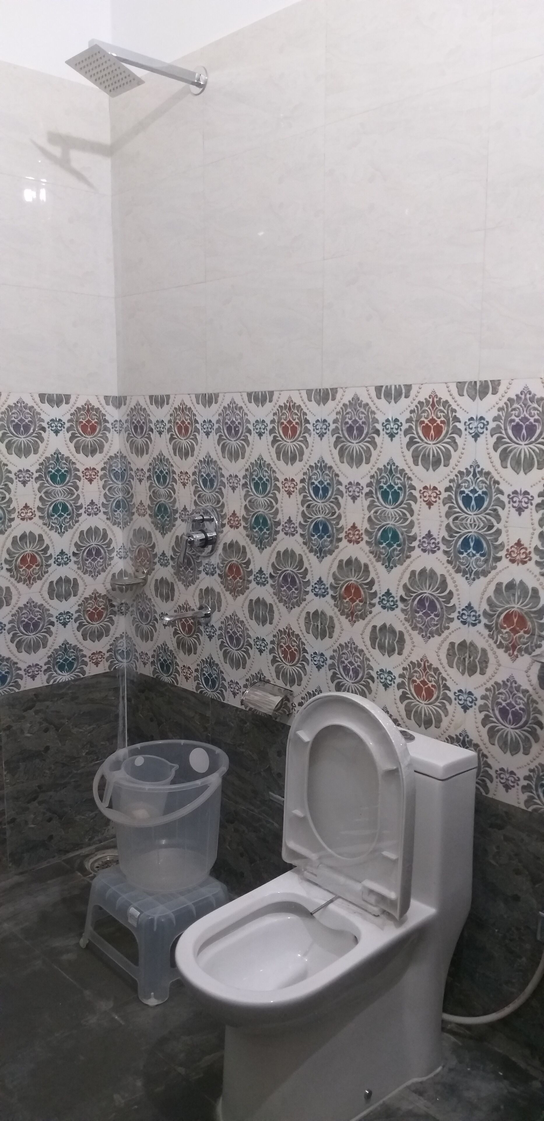 A bathroom with a toilet, a shower, and a bidet. The walls are tiled with a floral pattern.