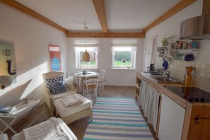 A cozy kitchen with wooden beams, a dining area with a table and chairs, and a view of the garden through the windows. - Vacation EXTRA TIME HOLIDAY (Hasselberg)