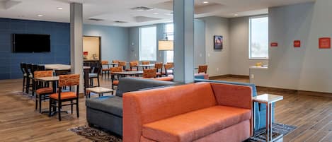 A modern hotel lobby with a seating area, a flat-screen TV, and a large window providing natural light.