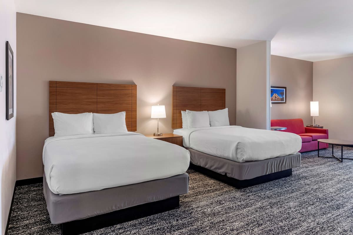 A hotel room with two beds, a red sofa, and a small table.