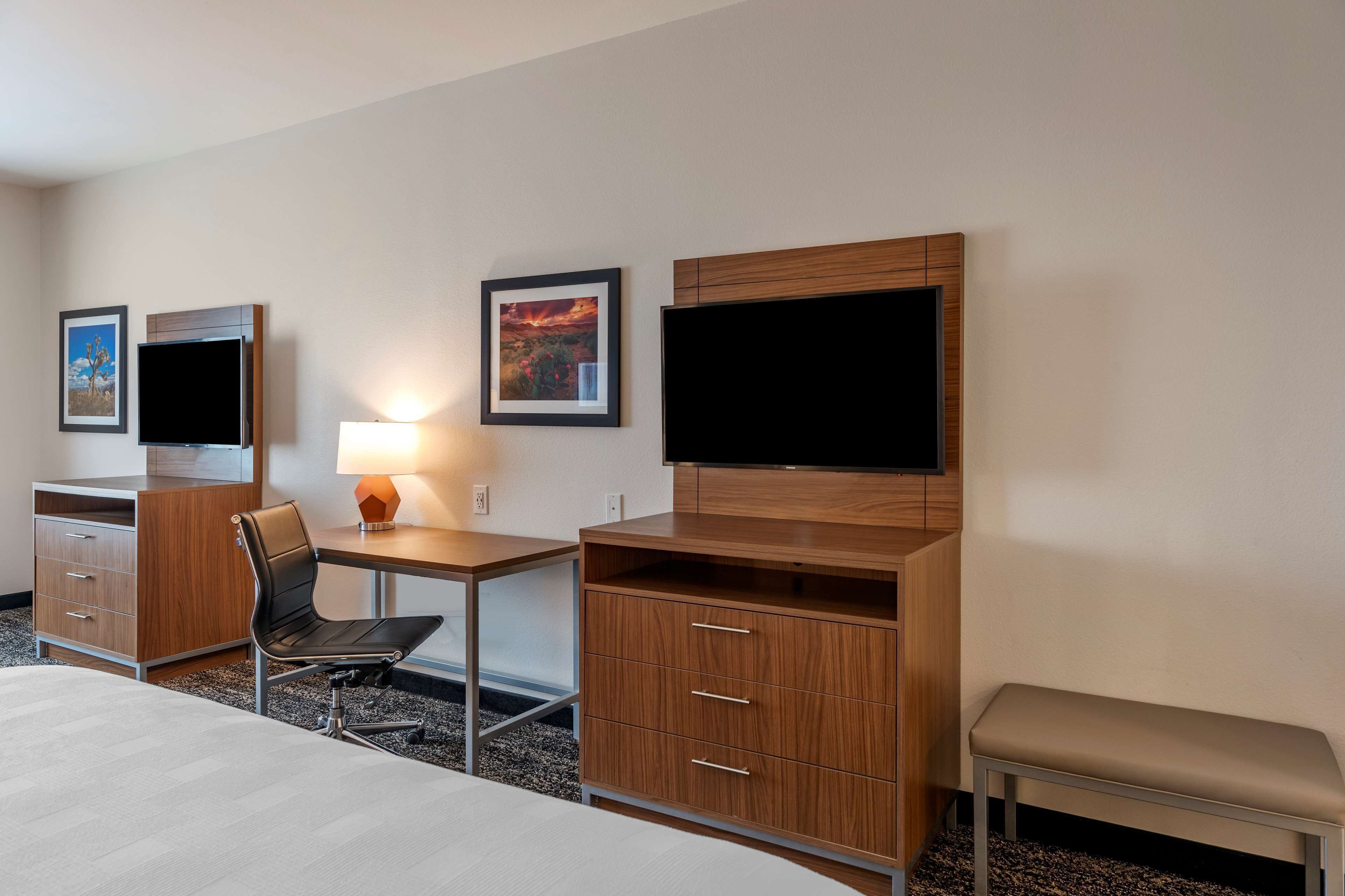 Habitación de hotel con cama, escritorio y silla, televisor, mueble de madera y una banca.