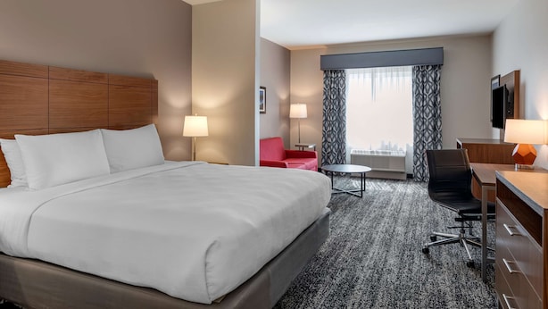 Ein Hotelzimmer mit einem großen Bett, einem Schreibtisch mit Stuhl, einem kleinen Tisch und einem roten Sessel.