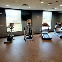 Un gimnasio con máquinas de cardio, un televisor en la pared y amplias ventanas.