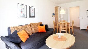 A modern living room with a sofa, a round table, and a dining area with chairs. There are two framed pictures on the wall. - Dünenblick apartment DBL02, house 1 (Ostseebad Boltenhagen)