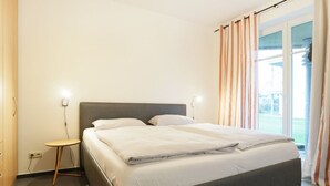 A hotel room with a bed, bedside table, lamp, and a view of the outdoors through a window. - Dünenblick apartment DBL02, house 1 (Ostseebad Boltenhagen)