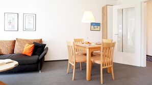 A living room with a sofa, a dining table with chairs, a lamp, and framed pictures on the wall. - Dünenblick apartment DBL02, house 1 (Ostseebad Boltenhagen)