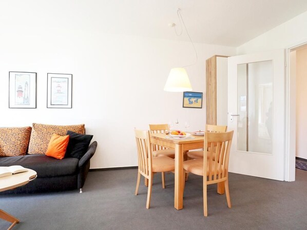 A living room with a sofa, a dining table with chairs, a lamp, and framed pictures on the wall.