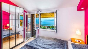 Une chambre à coucher comprenant un lit, une table de chevet, une lampe, une porte-fenêtre coulissante et une vue sur la mer.