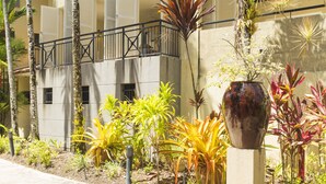 Un immeuble à plusieurs étages doté de balcons, entouré de plantes tropicales et de palmiers.