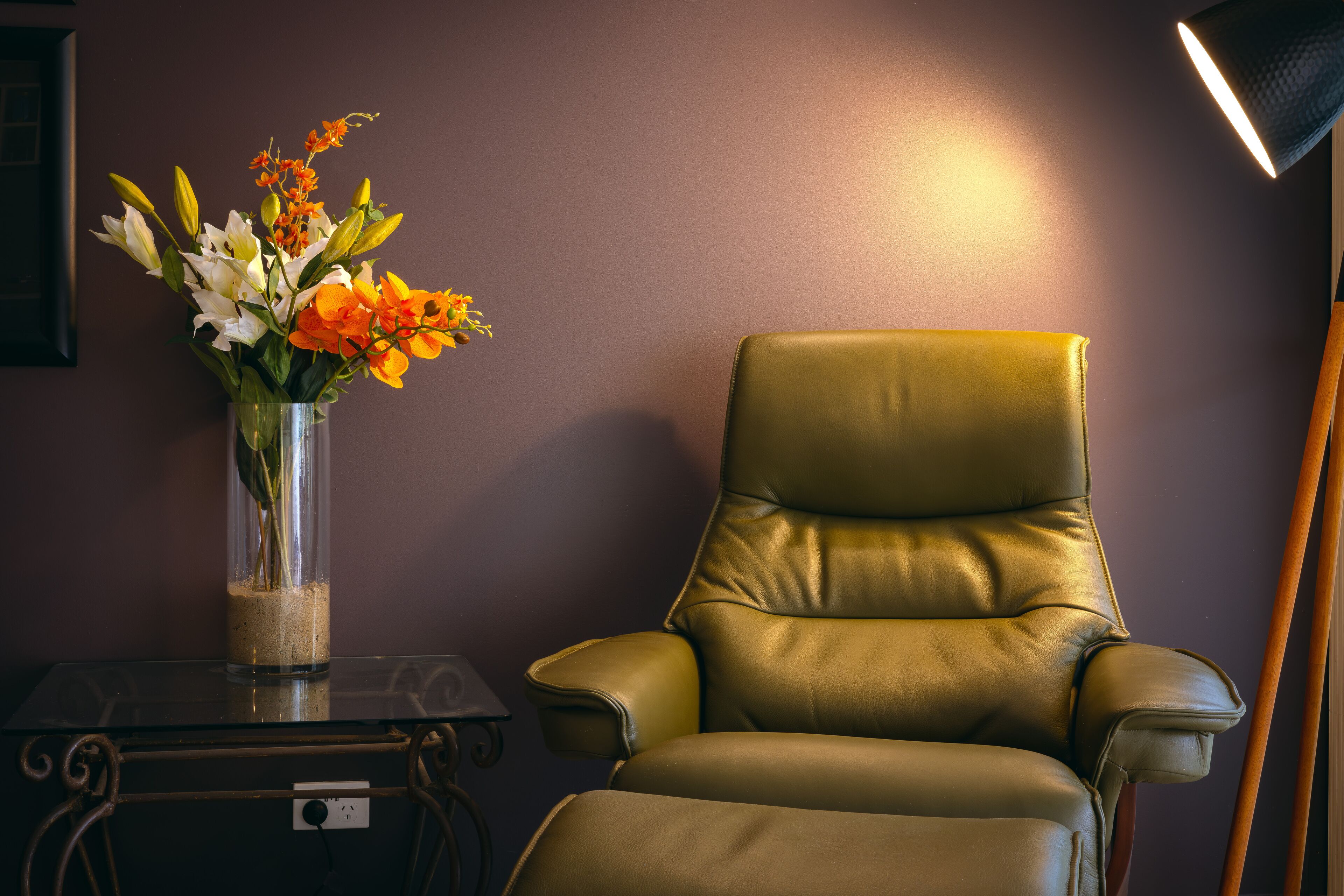 A room with a leather armchair, a glass vase with flowers, and a table with a power outlet.