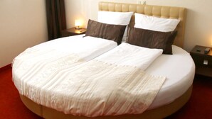 A large bed with a tufted headboard, two pillows, and a bedside table with a lamp. - Junior suite with bath - Home Hotel (Wilhelmshaven)