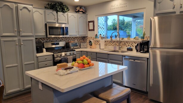 A modern kitchen with a central island, stainless steel appliances, and a view to the outdoors. - Kids Love Us! Legoland Home with A Pool (Oceanside)