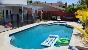 A rectangular swimming pool with a built-in slide, surrounded by a fence, and equipped with an inflatable float. - Kids Love Us! Legoland Home with A Pool (Oceanside)