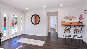 A spacious room with a dark wooden floor, a white door with glass panels, a round mirror, and a small wooden table with two stools. - Kids Love Us! Legoland Home with A Pool (Oceanside)