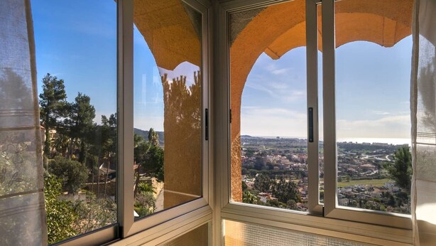 Quarto com amplas janelas que oferecem vista para a cidade e áreas verdes.