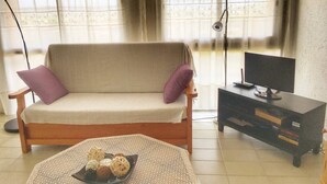 Uma sala de estar com sofá, televisão sobre um suporte e uma luminária.