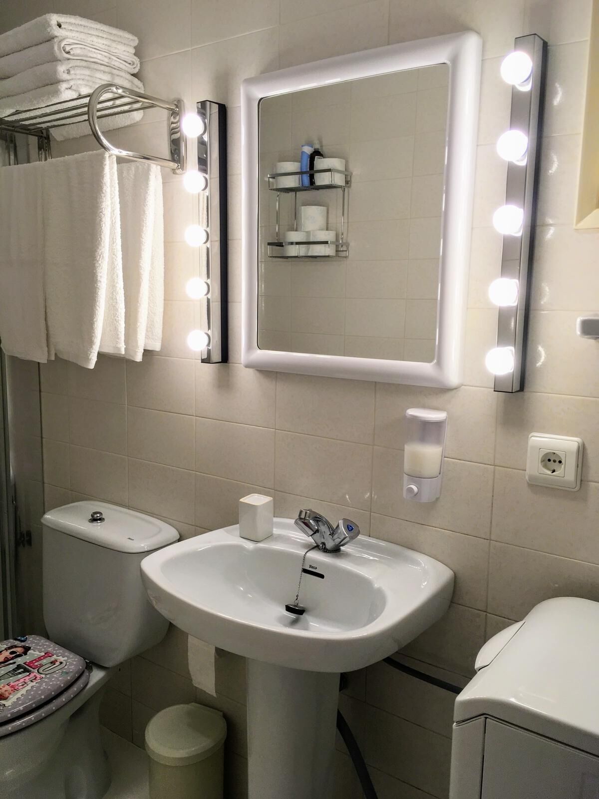 A bathroom with a sink, toilet, and a vanity mirror with lights.